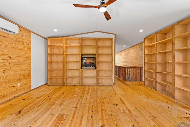 unfurnished living room with lofted ceiling, ceiling fan, wooden walls, a wall mounted air conditioner, and light wood-type flooring