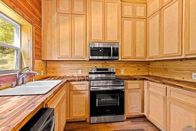 kitchen with butcher block counters, light brown cabinetry, sink, appliances with stainless steel finishes, and hardwood / wood-style floors