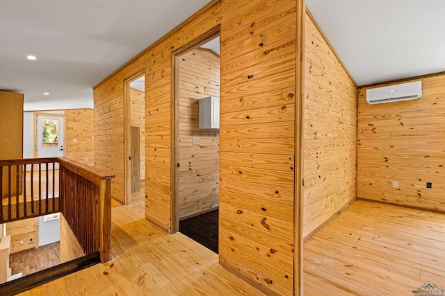 hall with light wood-type flooring, a wall unit AC, and wood walls