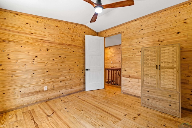 unfurnished bedroom featuring ceiling fan, lofted ceiling, wooden walls, and light wood-type flooring