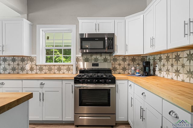 kitchen with butcher block countertops, appliances with stainless steel finishes, white cabinets, and tasteful backsplash