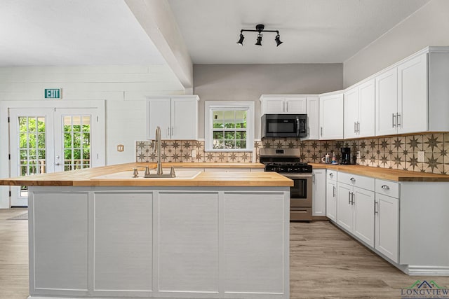 kitchen featuring stainless steel range with gas stovetop, a sink, white cabinets, and wooden counters