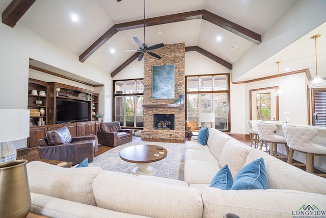 living room with ceiling fan, hardwood / wood-style floors, beam ceiling, high vaulted ceiling, and a fireplace