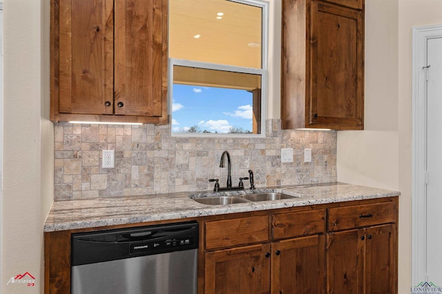 kitchen with light stone counters, a sink, decorative backsplash, stainless steel dishwasher, and brown cabinets