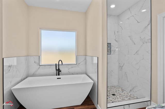 bathroom with a freestanding tub, a wainscoted wall, a walk in shower, wood finished floors, and tile walls