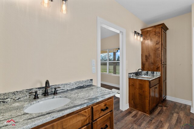 bathroom featuring a sink, baseboards, two vanities, and wood finished floors