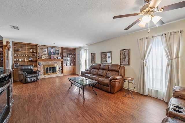 living room featuring a brick fireplace, hardwood / wood-style floors, built in features, and a textured ceiling