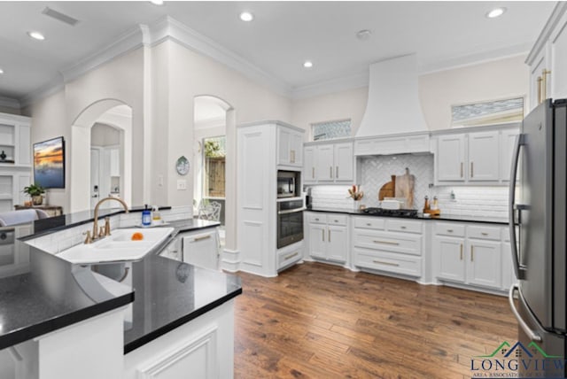 kitchen with decorative backsplash, stainless steel appliances, white cabinets, and custom exhaust hood