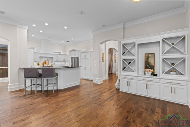 kitchen with stainless steel fridge, a kitchen bar, white cabinetry, and crown molding