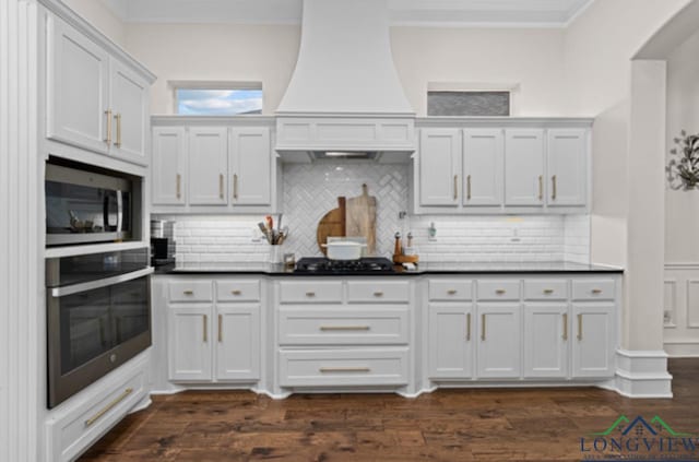 kitchen with tasteful backsplash, white cabinets, stainless steel appliances, and custom range hood