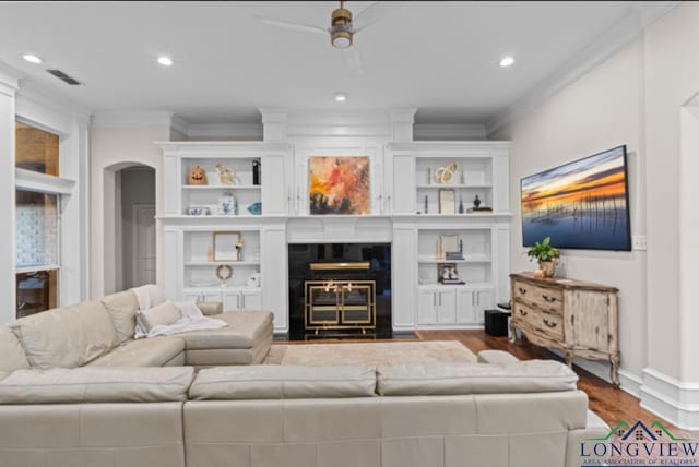 living room with built in shelves, ceiling fan, crown molding, wood-type flooring, and a fireplace