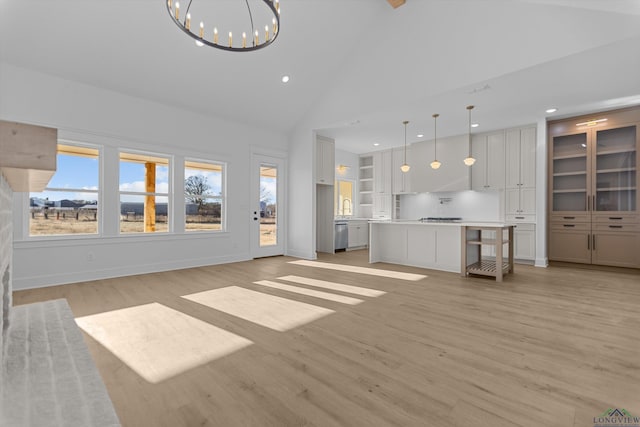 unfurnished living room featuring light wood-style flooring, an inviting chandelier, high vaulted ceiling, a sink, and recessed lighting