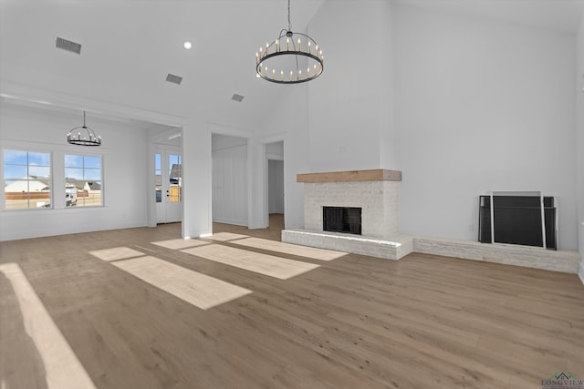 unfurnished living room with light wood-type flooring, a brick fireplace, visible vents, and a chandelier