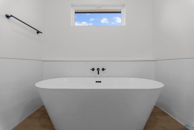 bathroom with wood finished floors, wainscoting, a freestanding tub, and tile walls