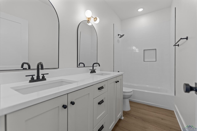 full bath featuring toilet, double vanity, a sink, and wood finished floors