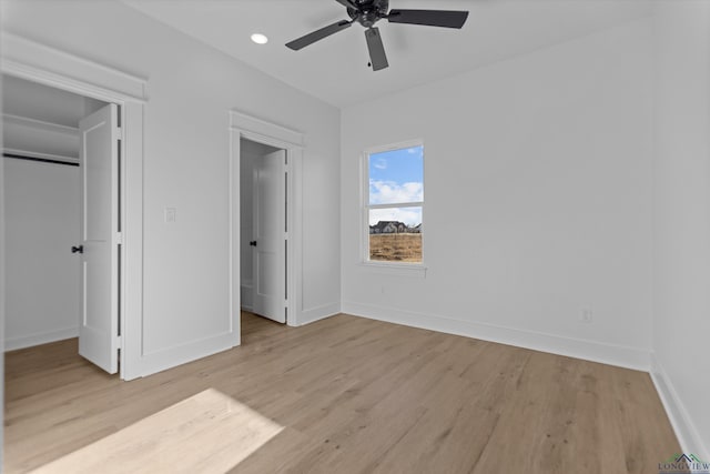 unfurnished bedroom with baseboards, light wood-style flooring, ceiling fan, a walk in closet, and recessed lighting