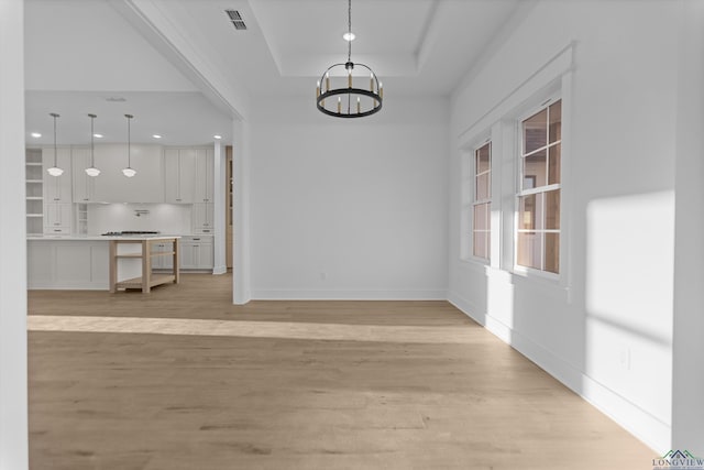 unfurnished dining area featuring visible vents, a raised ceiling, baseboards, light wood-style flooring, and an inviting chandelier