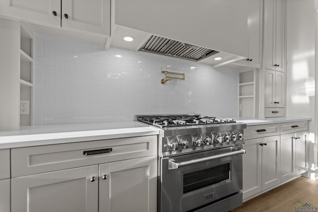 kitchen with tasteful backsplash, stainless steel range, wood finished floors, light countertops, and white cabinetry