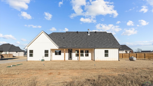 back of property featuring a shingled roof, fence, and a lawn