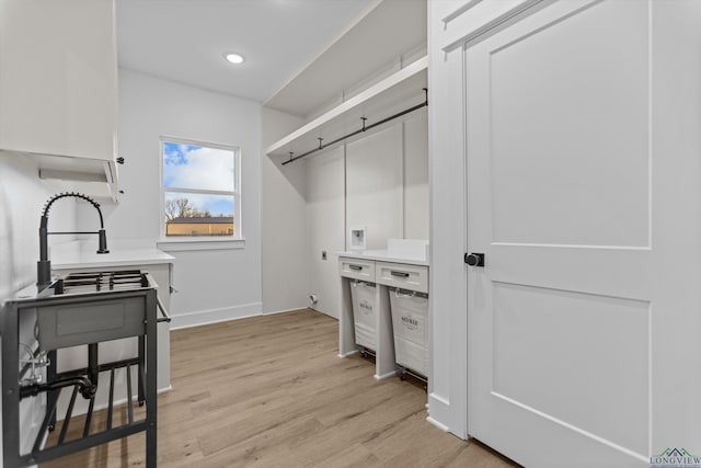 interior space featuring light wood-style flooring, recessed lighting, hookup for an electric dryer, baseboards, and cabinet space