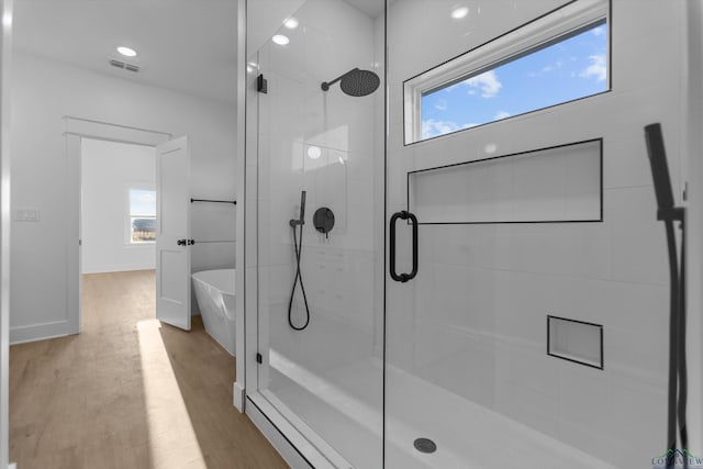 full bathroom featuring plenty of natural light, visible vents, a soaking tub, wood finished floors, and a shower stall