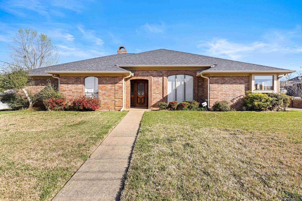 rear view of property with roof with shingles, brick siding, a patio, a chimney, and a lawn