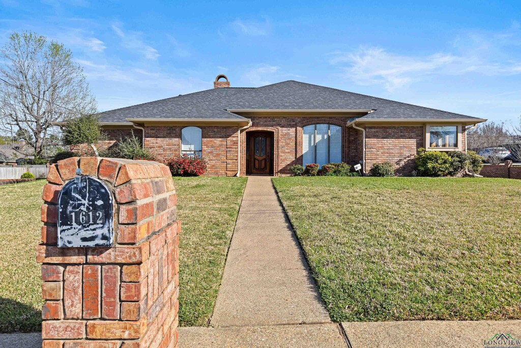 single story home with roof with shingles, a front yard, a chimney, and brick siding