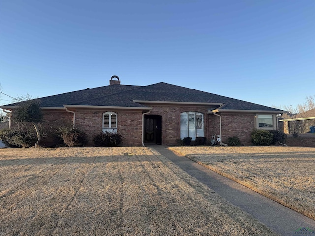 single story home with roof with shingles, a front yard, a chimney, and brick siding