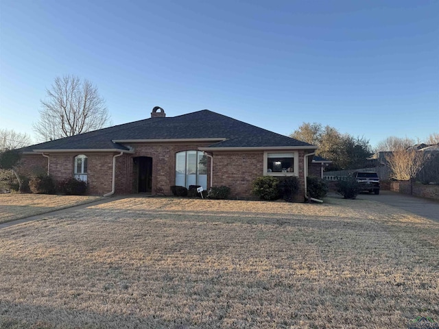 ranch-style home featuring a shingled roof, a chimney, a front lawn, and brick siding