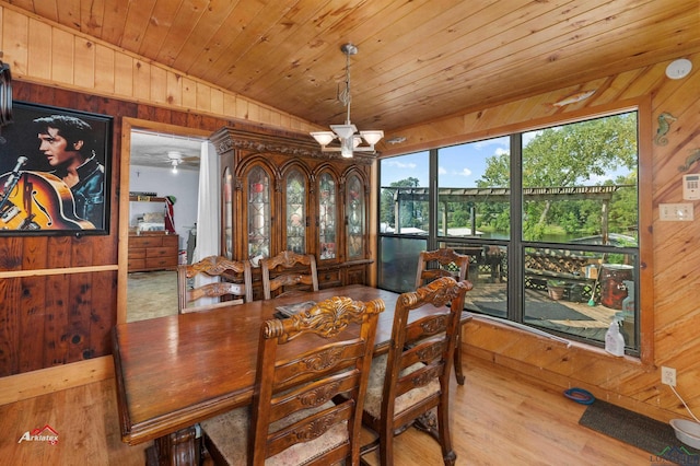 dining area featuring light wood-type flooring, wooden walls, an inviting chandelier, and vaulted ceiling