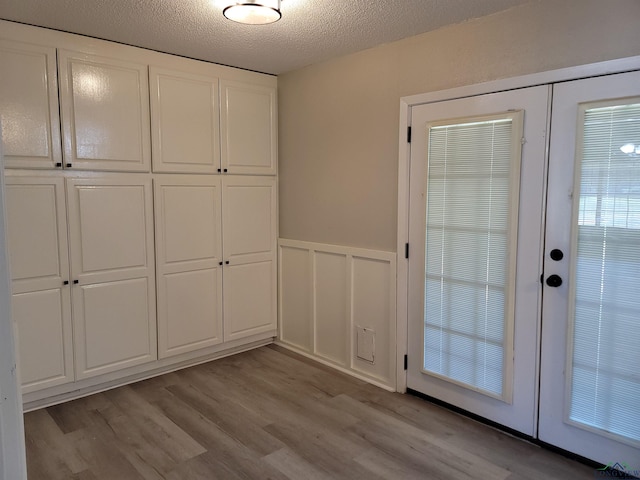 711 Wildwood Rd, Daingerfield, TX 75638 - doorway to outside featuring wainscoting, light wood-style flooring, a decorative wall, a textured ceiling, and french doors