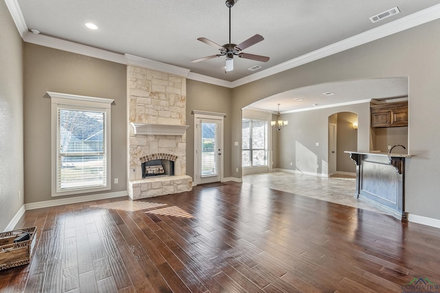 unfurnished living room featuring ceiling fan with notable chandelier, crown molding, a fireplace, and wood-type flooring