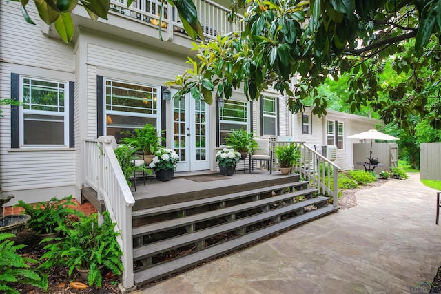 view of exterior entry with french doors, a deck, a patio area, fence, and a balcony