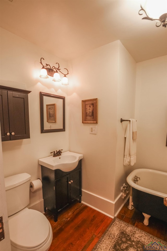 full bathroom with a freestanding bath, wood finished floors, baseboards, vanity, and toilet