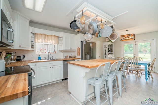 kitchen with open shelves, white cabinets, stainless steel appliances, and butcher block counters