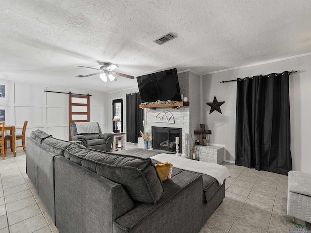 tiled living room featuring a textured ceiling, ceiling fan, crown molding, a barn door, and a fireplace