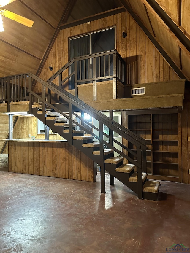 stairs with lofted ceiling, concrete flooring, and wood walls