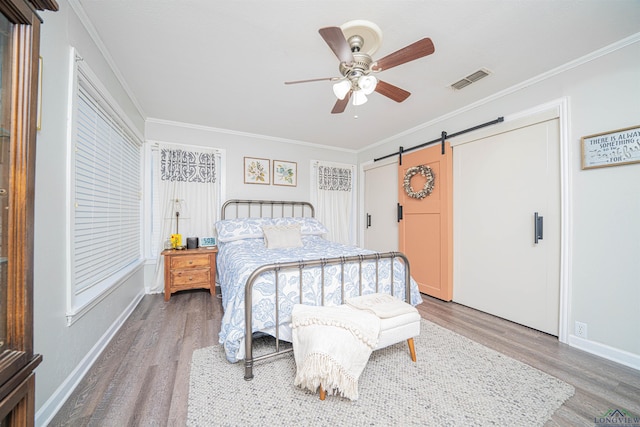 bedroom featuring wood-type flooring, ornamental molding, a barn door, and ceiling fan