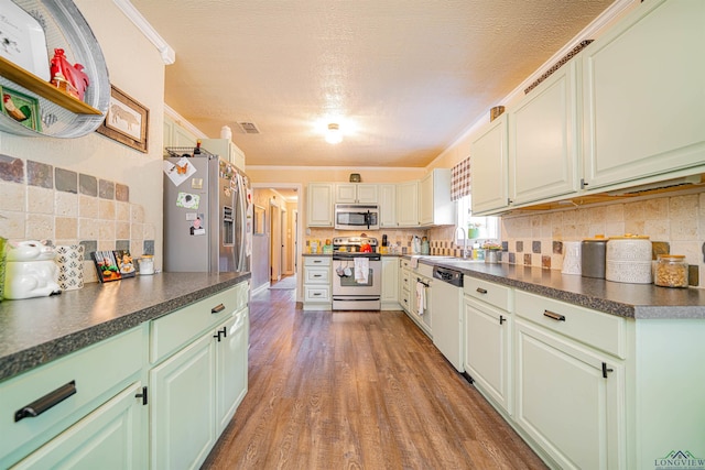 kitchen with sink, tasteful backsplash, wood-type flooring, ornamental molding, and appliances with stainless steel finishes