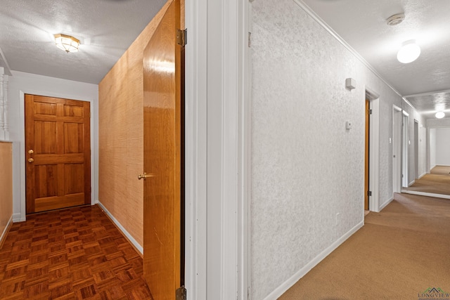 hall featuring a textured ceiling, baseboards, and ornamental molding