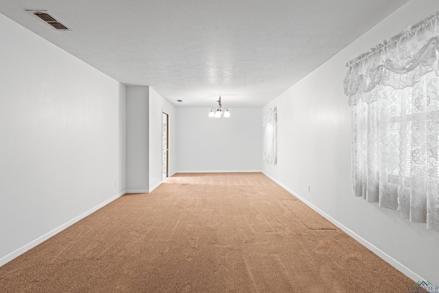 spare room featuring light colored carpet, a chandelier, and baseboards