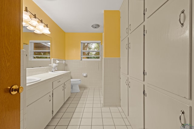full bathroom with tile walls, toilet, tile patterned flooring, wainscoting, and double vanity