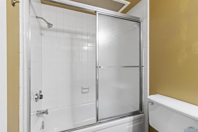 bathroom featuring toilet and shower / bath combination with glass door