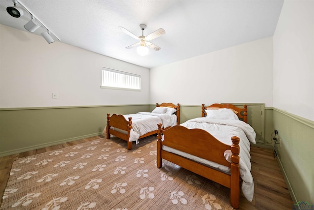 bedroom with rail lighting, baseboards, ceiling fan, and wood finished floors