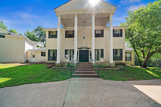 greek revival inspired property featuring a front lawn and brick siding
