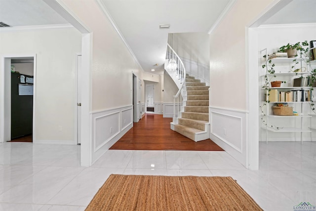 tiled foyer entrance featuring stairway, a decorative wall, wainscoting, and ornamental molding