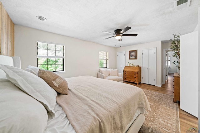 bedroom featuring visible vents, two closets, a textured ceiling, light wood-style floors, and ceiling fan
