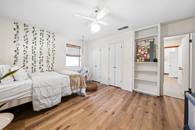 bedroom with light wood finished floors, visible vents, two closets, baseboards, and ceiling fan