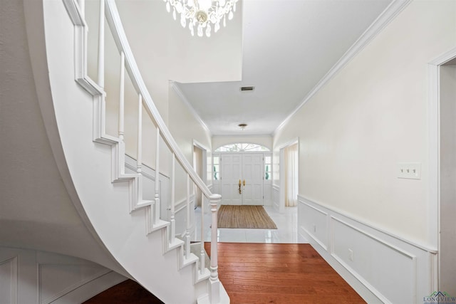 foyer entrance featuring a decorative wall, crown molding, visible vents, and a wainscoted wall