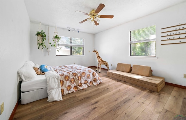 bedroom with baseboards, multiple windows, hardwood / wood-style floors, and track lighting